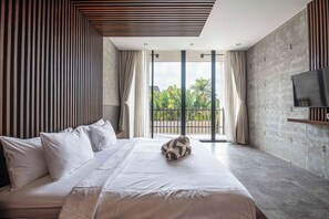 Una camera d'albergo moderna con un letto grande, una TV a schermo piatto e un balcone vista verde.
