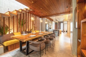A modern dining area with a wooden table, cushioned chairs, and pendant lighting.