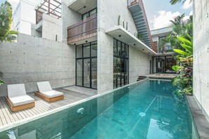 Ein moderner Poolbereich im Freien mit zwei Liegestühlen, einer Betonplattform und einem balkongelassenen Glasbereich.