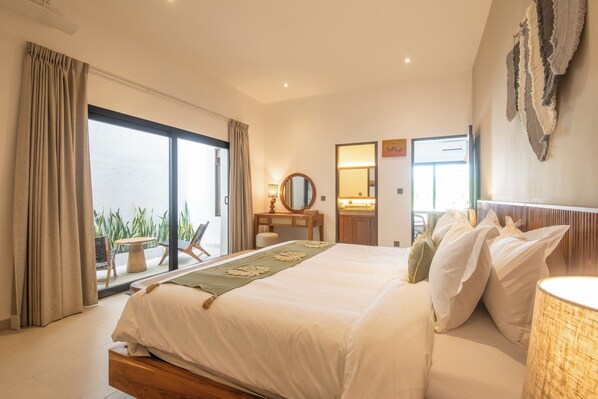 A modern hotel room with a large bed, a sitting area with a table and chairs, a bathroom with a mirror and sink, and a view of the sea through a sliding door. - 4 Bd Seminyak Rice Paddies View 4 Mins to Beach (Kerobokan)