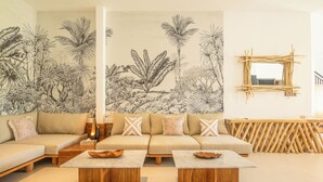 A modern living room with a beige sofa, two wooden coffee tables, and a large botanical mural on the wall. - 4 Bd Seminyak Rice Paddies View 4 Mins to Beach (Kerobokan)