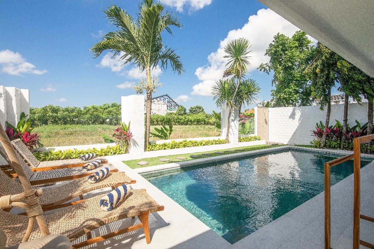 A pool area with lounge chairs, palm trees, and a view of a house in the background.
