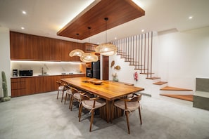 A modern kitchen with wooden cabinets, a large dining table, and a staircase. - Contemporary 5BR Luxury Villa 400m to the Sea (Seminyak)