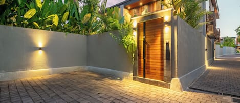 A modern house with a wooden door, a paved driveway, and a well-lit entrance.