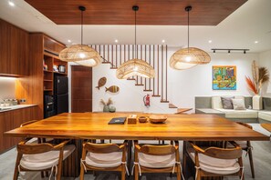 Une cuisine moderne avec des meubles en bois, une table à manger avec des chaises et un escalier agrémenté d’un mur décoratif.