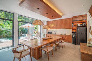 Une cuisine moderne avec une table à manger en bois, des chaises et des luminaires suspendus.