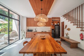 A modern kitchen with a wooden dining table, built-in appliances, and a staircase. - Contemporary 5BR Luxury Villa 400m to the Sea (Seminyak)