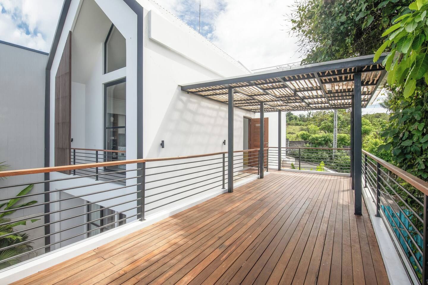 Una casa moderna con terraza de madera, un patio cubierto y vistas al verdor.