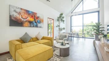 Uma sala de estar espaçosa, com um sofá amarelo, uma mesa de centro e um grande quadro abstrato.