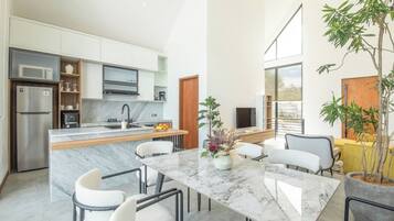 Una cocina moderna con una isla de mármol, muebles blancos y un refrigerador de acero inoxidable.