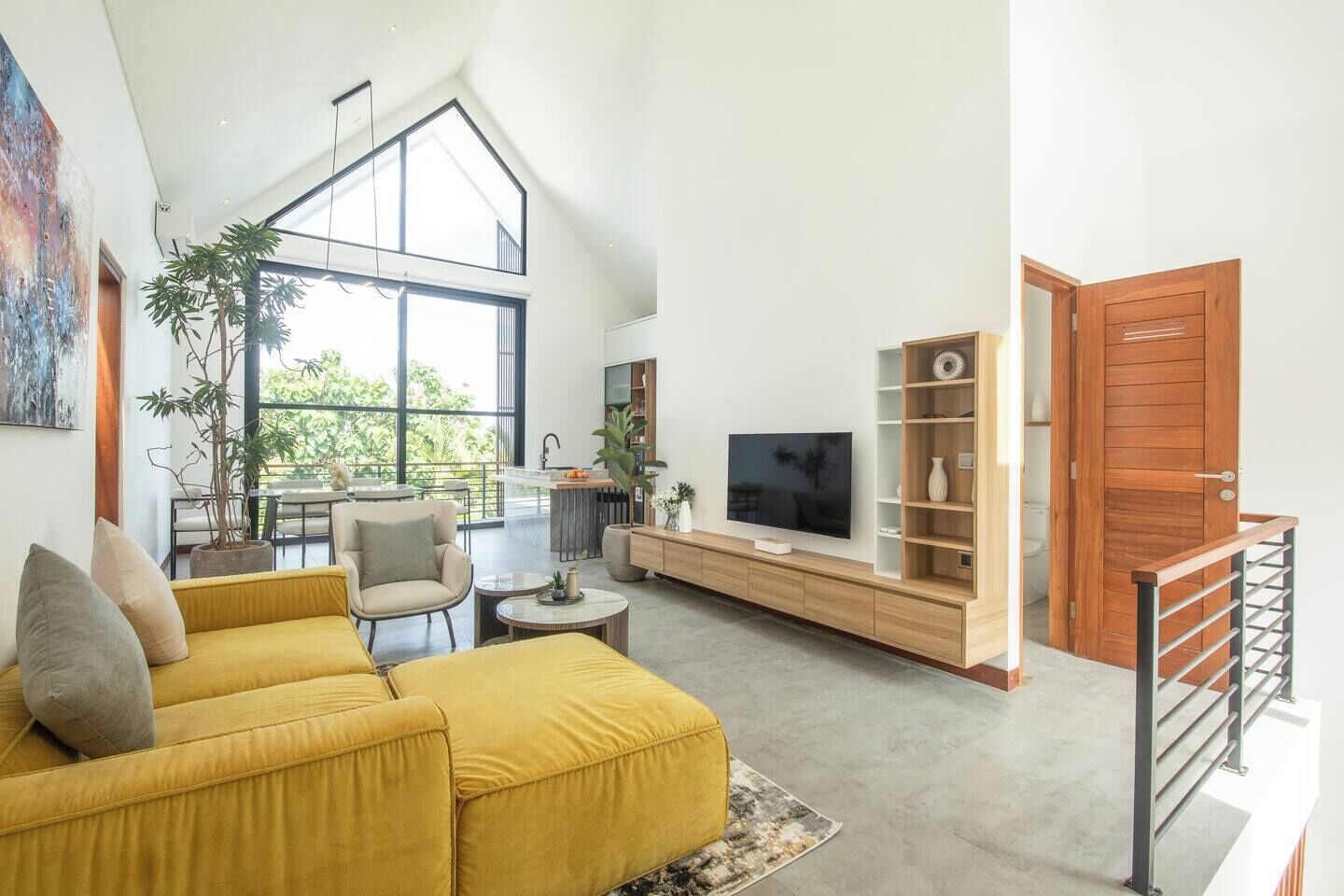 A spacious living area with a high ceiling, a yellow sofa, a TV, and a wooden bookshelf.