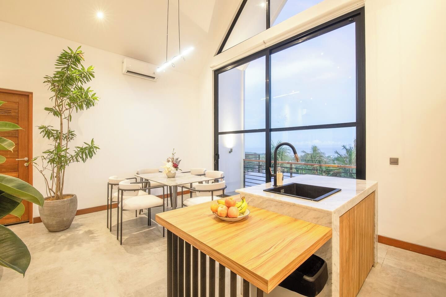 A modern kitchen with a large window, a dining area, and a potted plant.