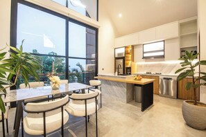A modern kitchen with a large island, white cabinetry, and a view of greenery outside. - Elegant Villa Sinara 2BR With Sea View (Kutuh)