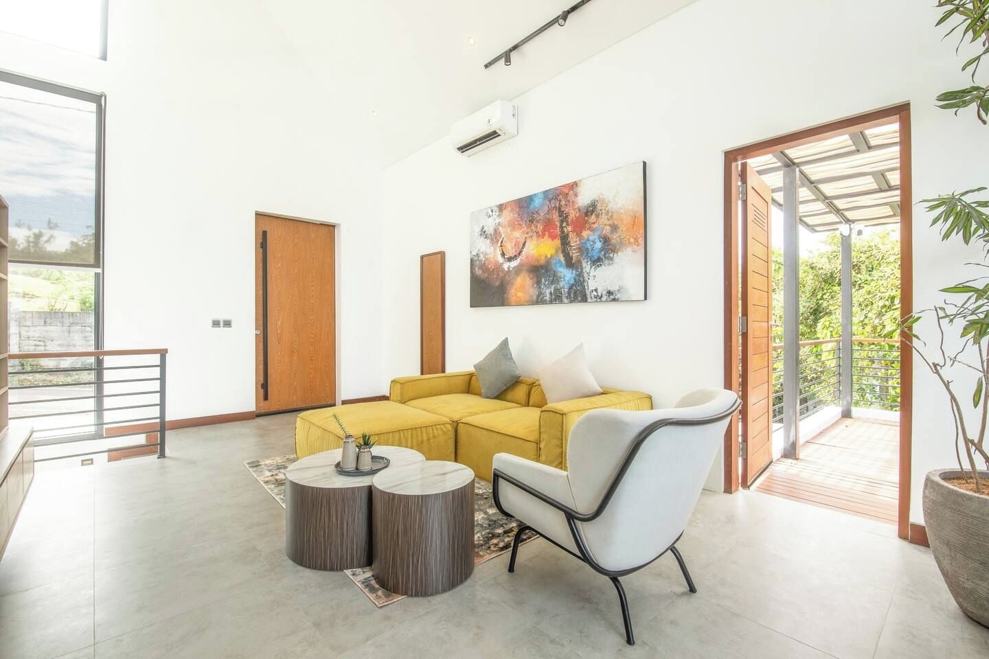 Una sala moderna con un sofá seccional amarillo, un sillón blanco y dos mesas redondas.