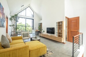 A spacious living area with a high ceiling, a yellow sofa, a TV, and a wooden bookshelf. - Elegant Villa Sinara 2BR With Sea View (Kutuh)