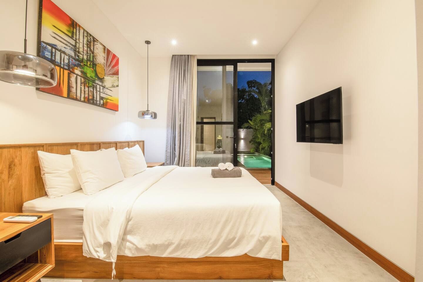 Ein modernes Hotelzimmer mit einem großen Bett, einem Flachbildfernseher, einem Gemälde an der Wand und Blick auf einen Außenpool.