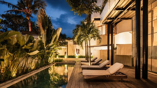 A wooden deck with lounge chairs and a pool, surrounded by tropical plants.