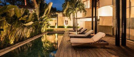 A wooden deck with lounge chairs and a pool, surrounded by tropical plants.