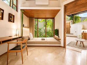 Una habitación con un escritorio de madera, un sofá y un televisor, y vistas a zonas verdes.