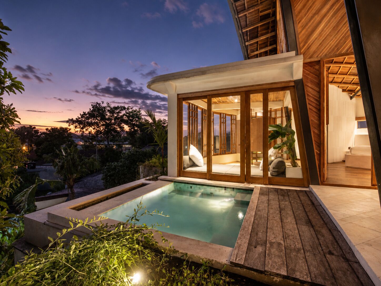 A modern house with a swimming pool, wooden deck, and glass doors leading to a living area.