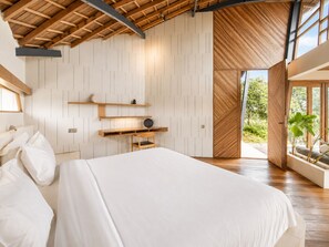 Une chambre avec un grand lit, des poutres en bois, un bureau et une vue sur la verdure.