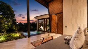 A modern outdoor living area with a pool, a sofa with cushions, and a wooden wall. - Stunning 2-br Penthouse With View 800m to Beach (Canggu)