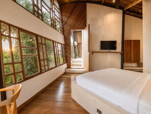 A bedroom with a large bed, a TV mounted on the wall, and a view of greenery through large windows. - Stunning 2-br Penthouse With View 800m to Beach (Canggu)