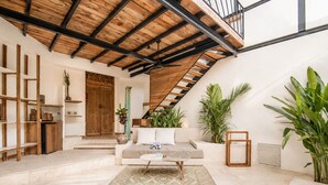 A spacious living area with a high ceiling, a built-in staircase, and a large window.
