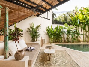 A modern outdoor living space with a pool, a sofa, a coffee table, and various plants. - Luxurious 1-br Villa With Pool, 800m to Echo Beach (Canggu)