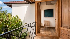Un balcón de madera con barandilla de metal, una puerta de madera y una silla.