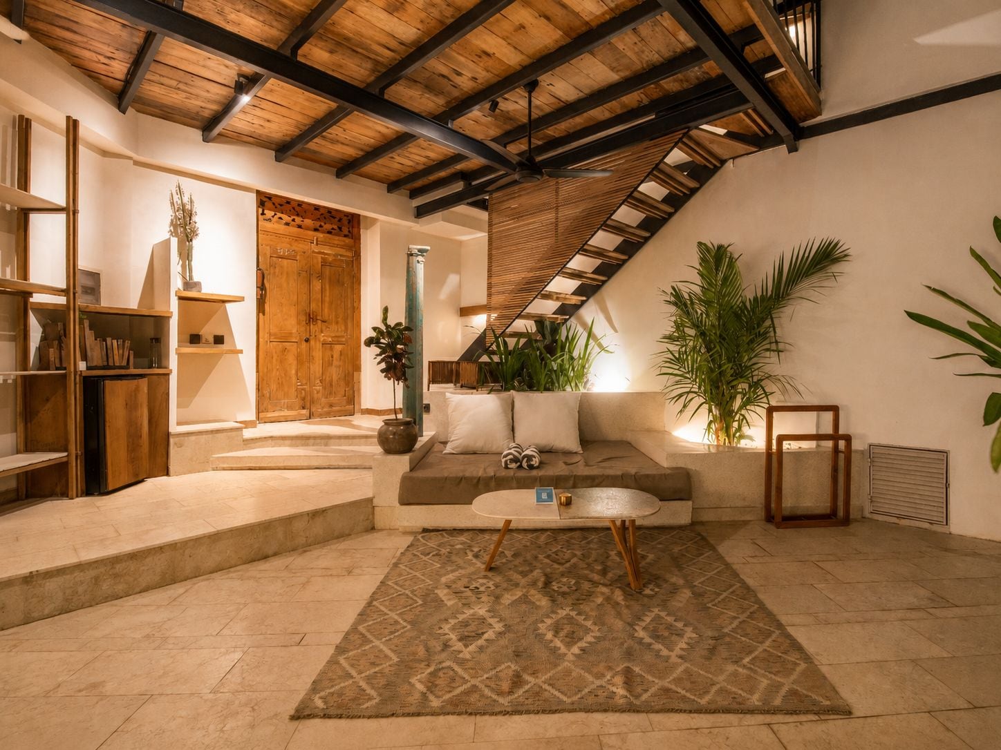 A cozy living area with a wooden ceiling, a sofa, a coffee table, and a large plant.