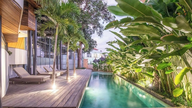 A wooden deck with lounge chairs and a swimming pool surrounded by tropical plants. - Exquisite 1-br Loft Art Deco Charm Shared Pool (Canggu)