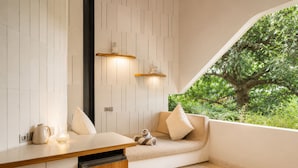 A modern room with a built-in bench, a wooden cabinet, and a view of greenery outside. - Exquisite 1-br Loft Art Deco Charm Shared Pool (Canggu)