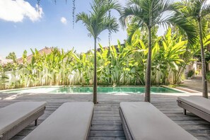 A poolside area with lounge chairs and tropical plants. - Exquisite 1-br Loft Art Deco Charm Shared Pool (Canggu)