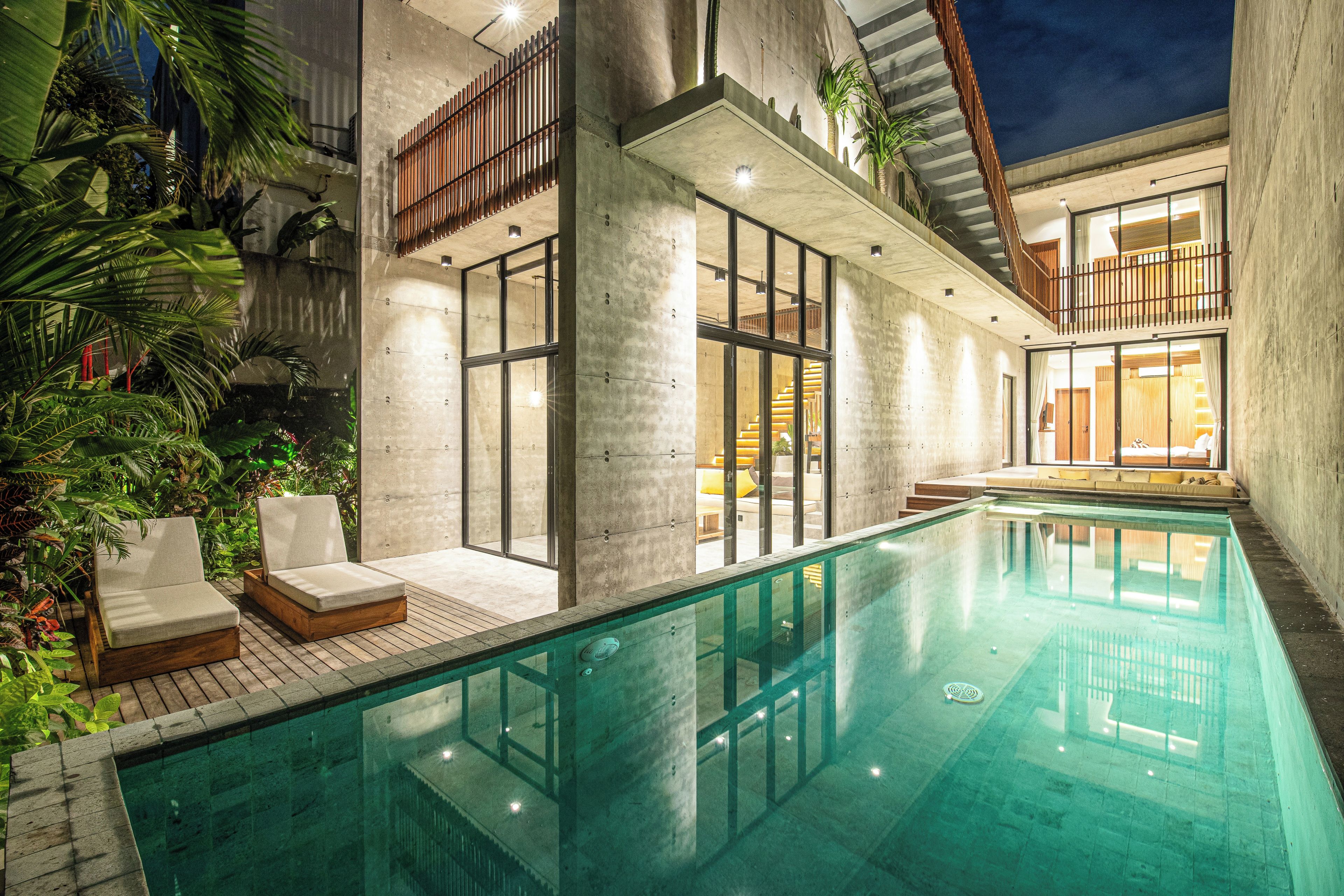 A modern indoor swimming pool with lounge chairs, concrete walls, and a wooden deck.