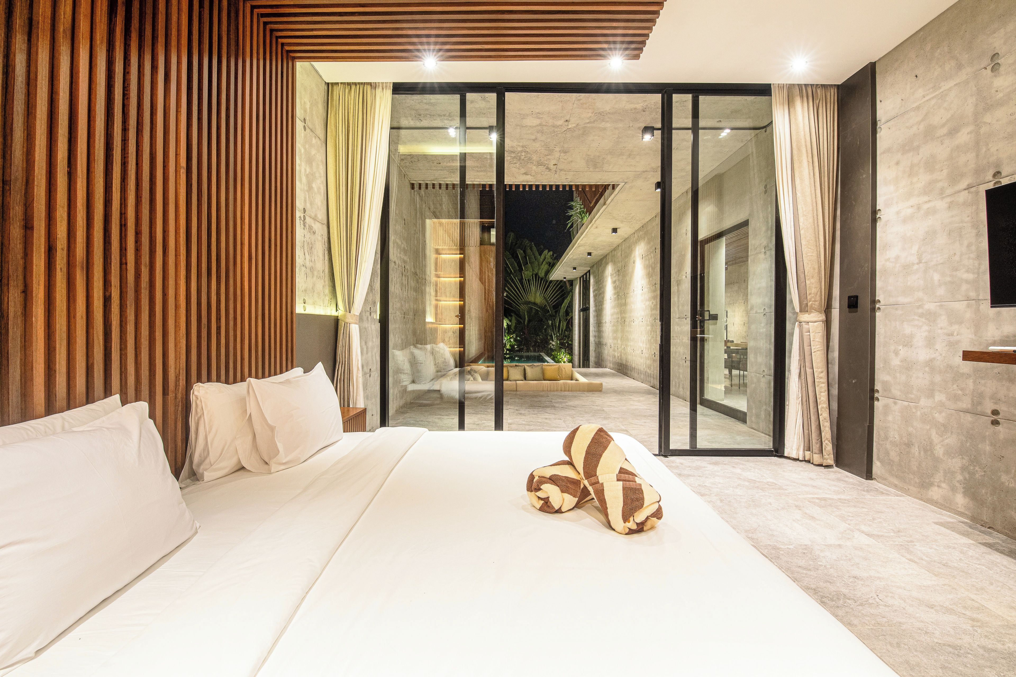 Ein modernes Schlafzimmer mit einem großen Bett, Schiebeglasfenstern, die auf einen Balkon führen, und einer Wand mit Holzlatten.