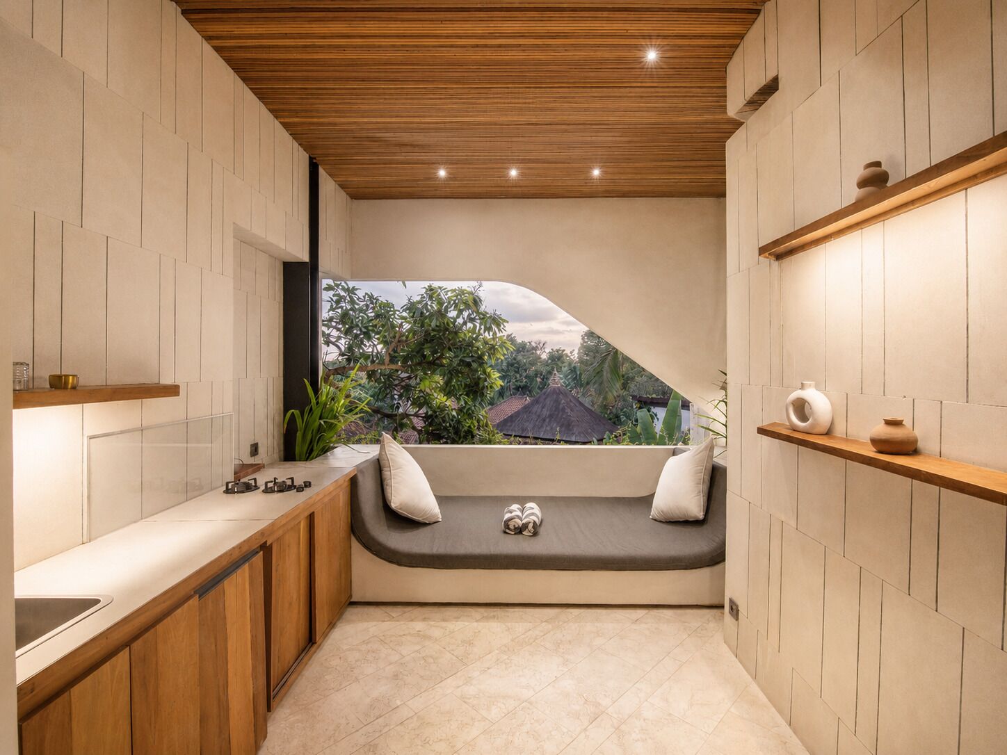 A modern kitchen with a built-in bench, wooden shelves, and a view of greenery outside.