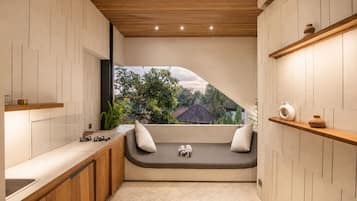 A modern kitchen with a built-in bench, wooden shelves, and a view of greenery outside.