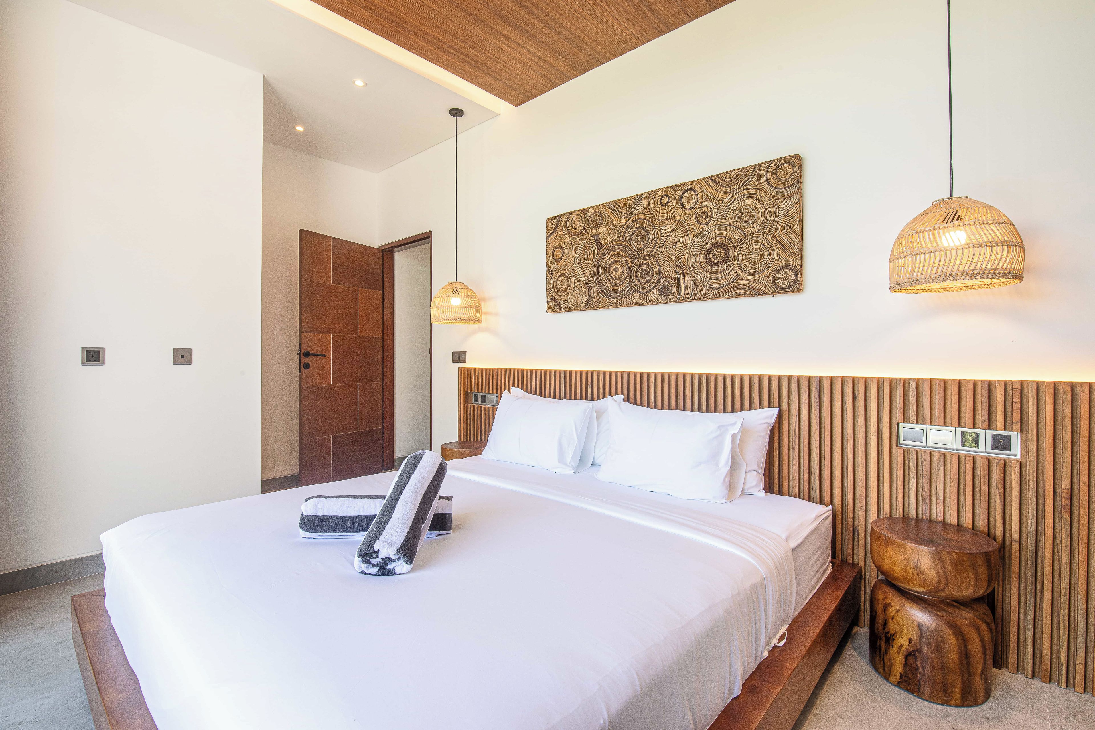 A modern hotel room with a large bed, wooden headboard, and a wall-mounted artwork.