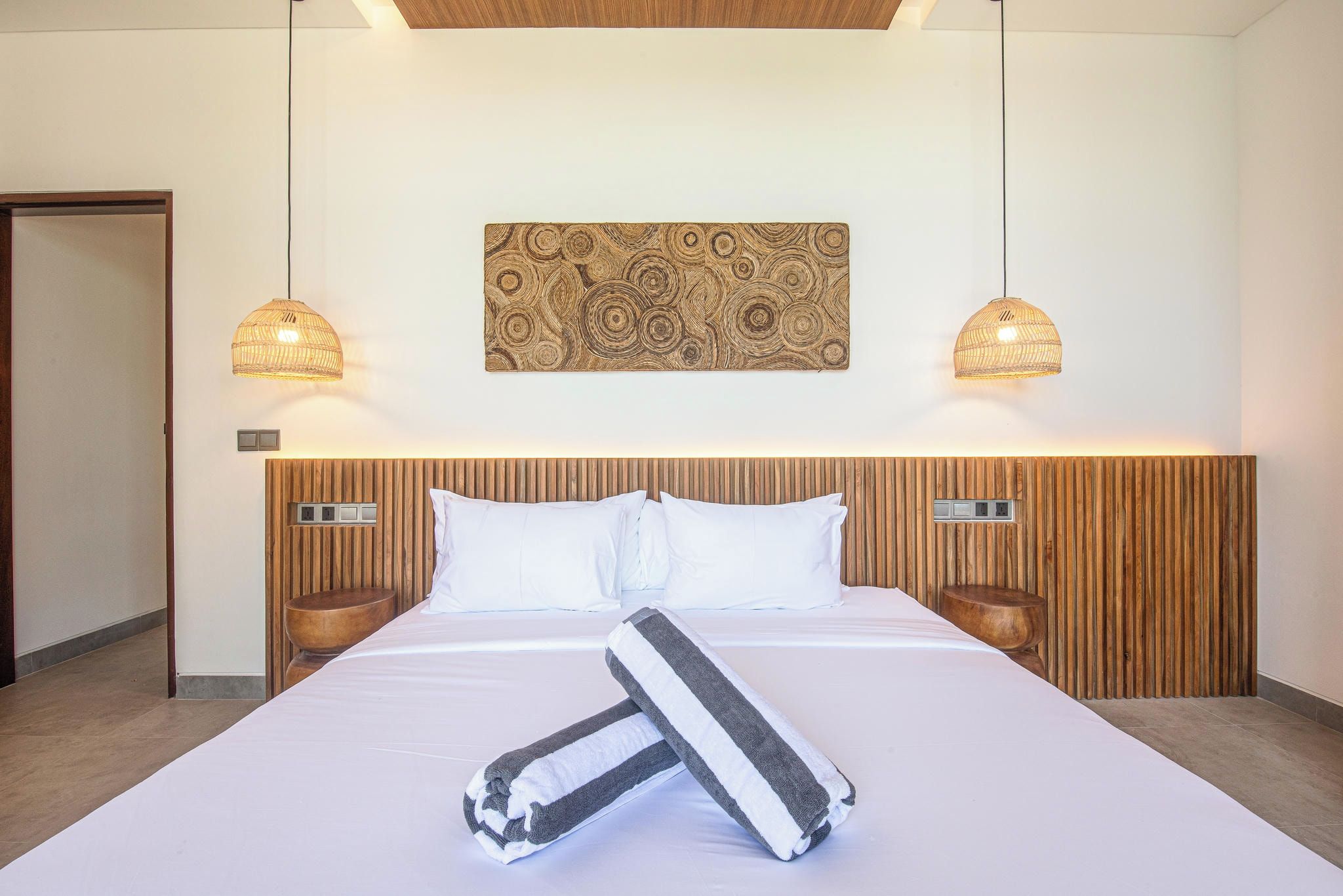 A hotel room with a large bed, two bedside lamps, a wooden headboard, and a wall-mounted artwork.