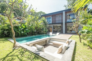 A modern house with a swimming pool, outdoor seating, and lush greenery.