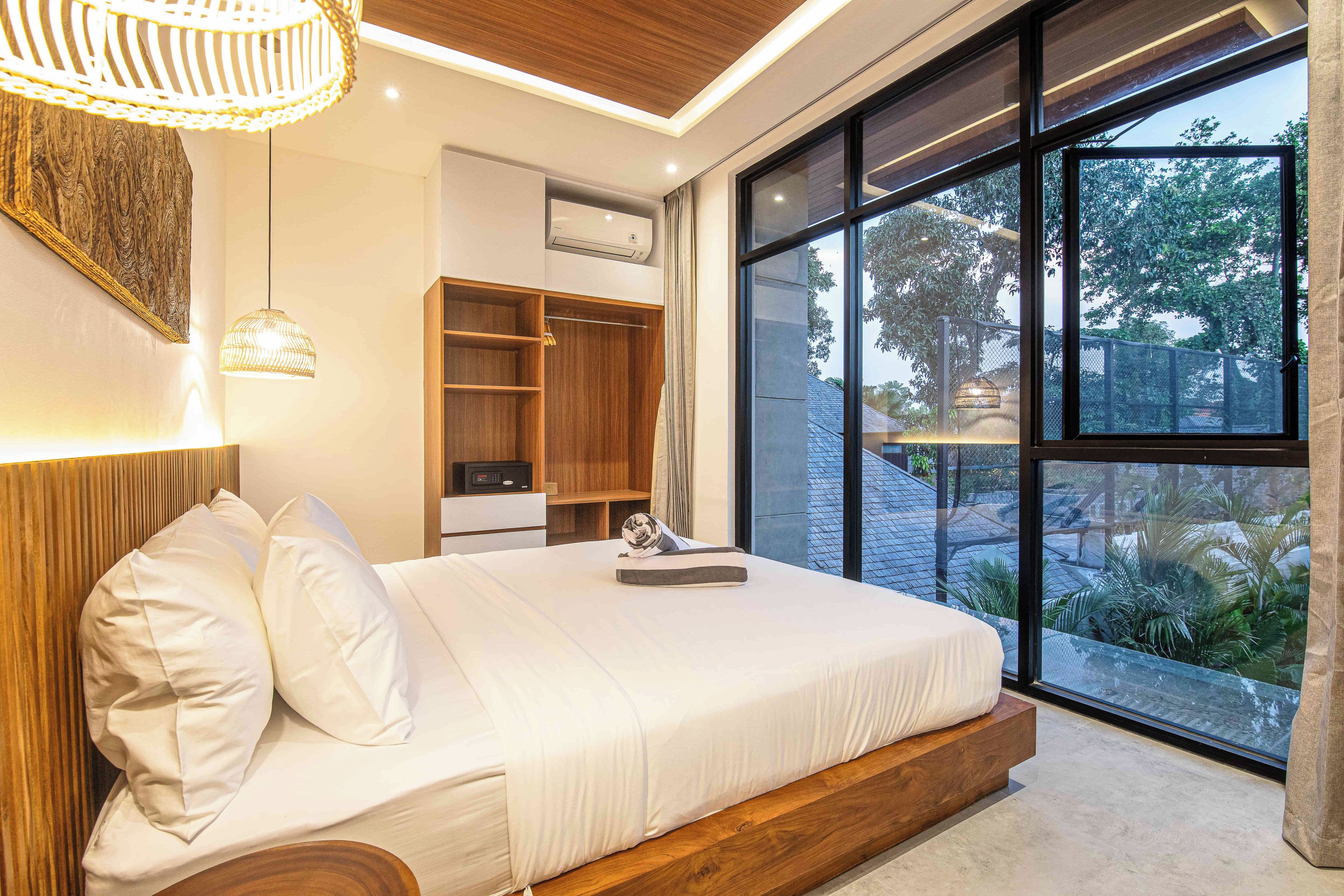 Een moderne slaapkamer met een groot bed, een inbouwkast en uitzicht op groen door grote ramen.