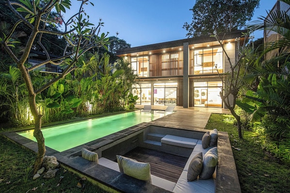A modern house with a swimming pool, outdoor seating, and lush greenery.