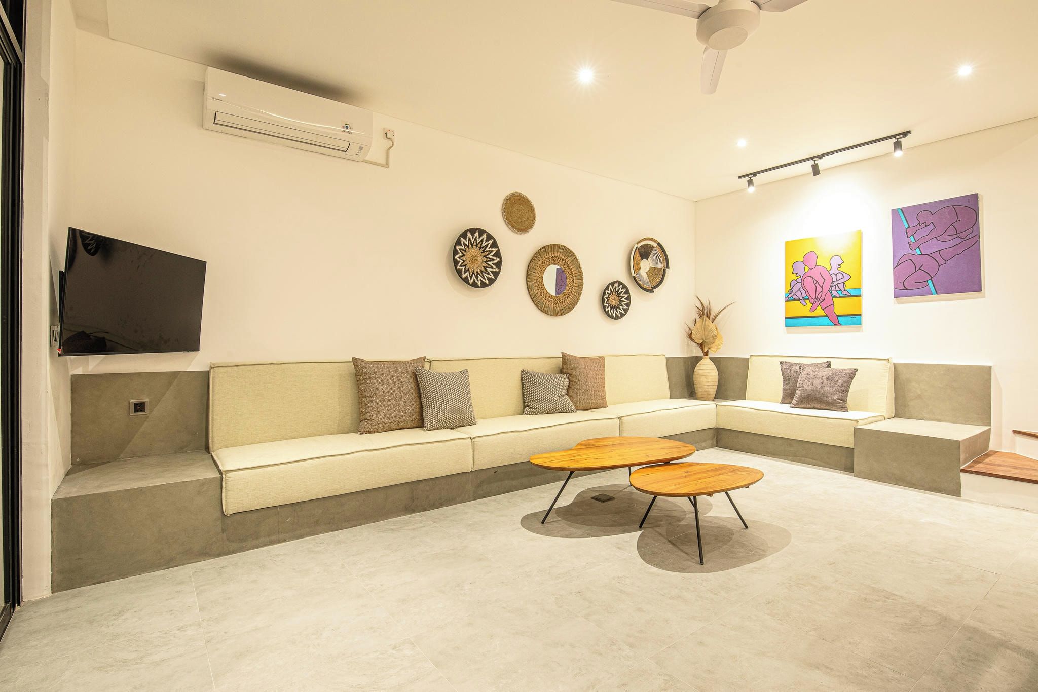 Un salon moderne avec un canapé d’angle, un téléviseur à écran plat, des œuvres d’art décoratives au mur et un ventilateur de plafond.