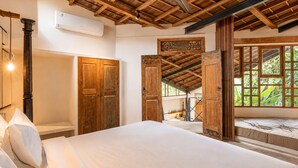A bedroom with a wooden ceiling, a bed, a wardrobe, and a window with a view of greenery. - Modern 2-br Art Deco Villa, 800m From the Beach (Canggu)