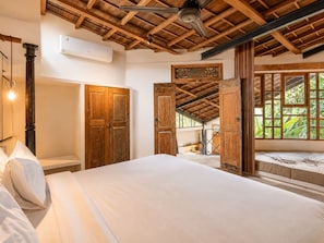 A bedroom with a wooden ceiling, a bed, a wardrobe, and a window with a view of greenery.