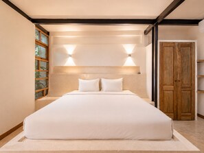 Een groot bed met twee kussens, een houten garderobe en een raam met zonwering.