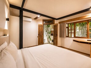Una camera da letto con un letto grande, una testata in legno, un comodino, uno specchio e una finestra con piante di bambù.