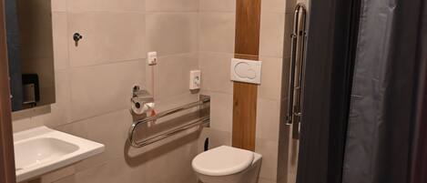 Un baño moderno con piso de madera, un lavamanos blanco, un inodoro, una ducha con cortina oscura y una barandilla.