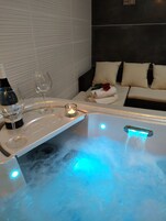 A spa area with a hot tub, a tray with a bottle of wine and a glass, and a candle.